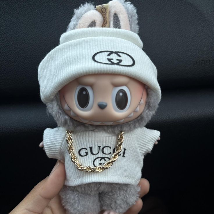 Toy figure wearing a Gucci outfit with a white beanie and sweater, held against a dark background.