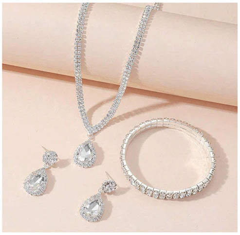 Silver jewelry set with necklace, bracelet, and earrings on a light pink background