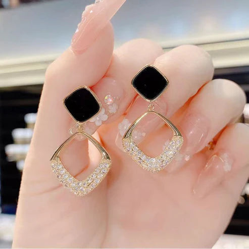 Gold earrings with black and clear stones held in a hand.
